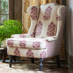 A Saanya Berry Chair by John Robshaw, an upholstered wing chair with a floral pattern in front of a window. - 30144956268590