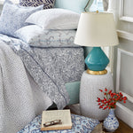 A bed adorned with John Robshaw's Organic Hand Stitched Light Indigo Quilt, hand-stitched with cotton voile, alongside a lamp. - 15564936380462