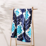 A blue and white Sashpura Indigo Beach Towel by John Robshaw hanging on a wooden rack. - 29274371653678