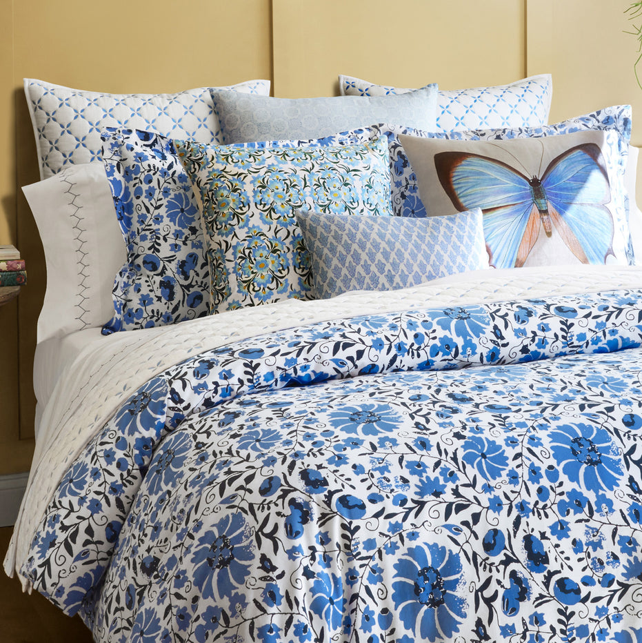A bed with blue and white Layla Azure Quilt bedding by John Robshaw and a butterfly pillow.