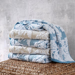 A stack of John Robshaw Pasak Blue Bath Towels on a wicker basket. - 28268378456110