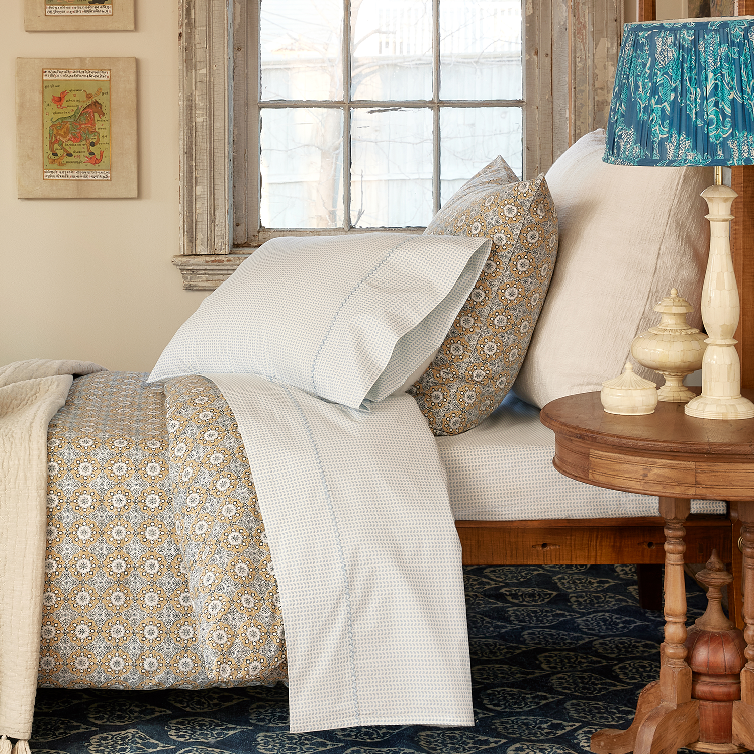 A John Robshaw Cinde Light Indigo Organic Sheet Set made of 100% cotton percale with a lamp on top of it.
