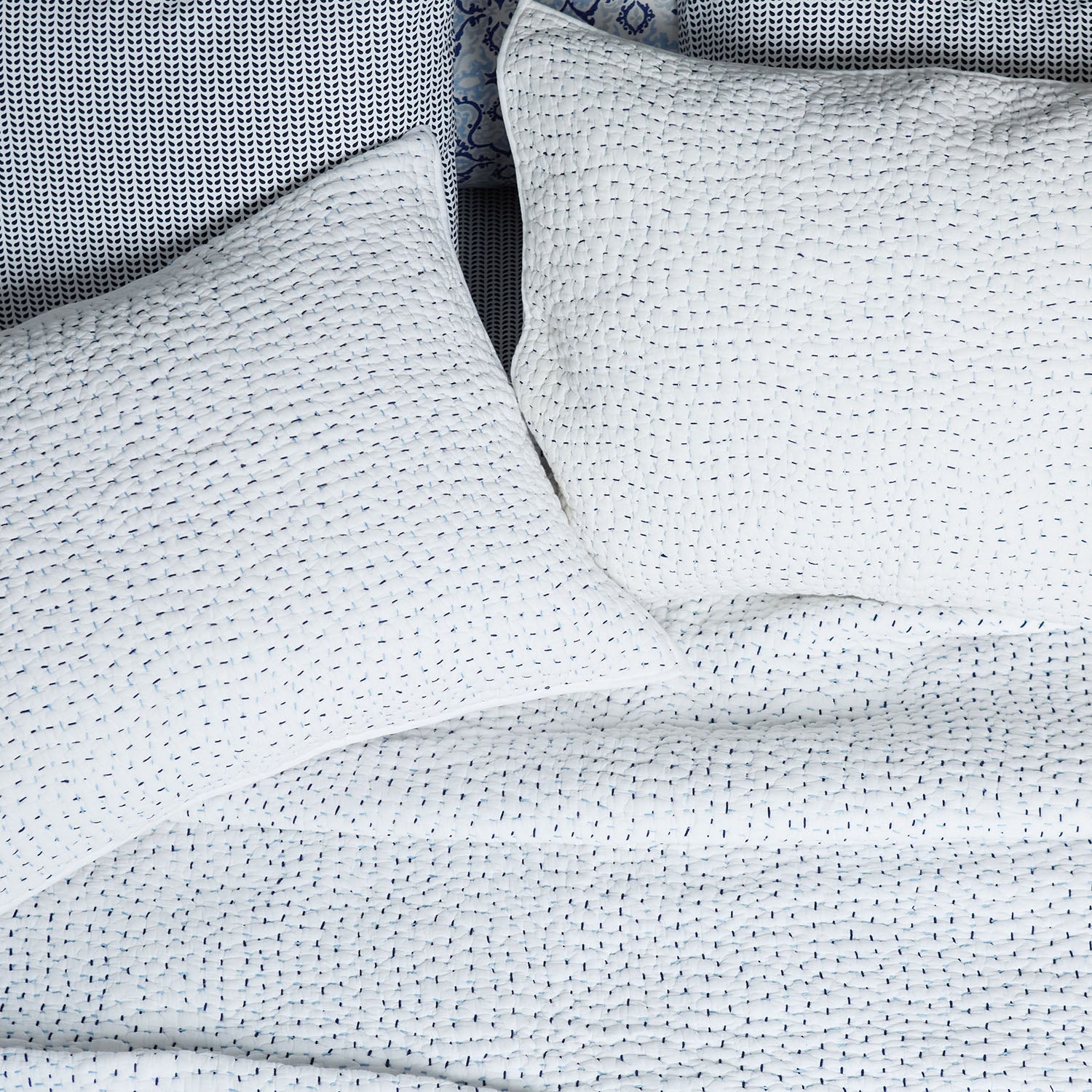 A bed with John Robshaw Organic Hand Stitched Light Indigo Quilt coverlets and blue and white polka dot pillows.