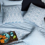 A bed with Kama Light Indigo Organic Sheet Set pillows, decorated with a bowl of fruit. - 28362868752430