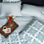 A bed with Sag Harbor Peacock Organic Sheets from John Robshaw, a tray of flowers, and a cup of coffee. - 28362871177262
