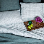 A Vivada Peacock Woven Quilt with blue and white pillows, hand stitching, and a tray of fruit. (Brand: Quilts & Coverlets) - 28362874257454