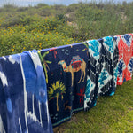 John Robshaw's Sashpura Indigo Beach Towel hanging on a fence in front of a beach in Uzbekistan. - 29542059245614