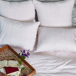 A cozy bed with John Robshaw's Organic Hand Stitched Lotus Quilt pillows and a book on top. - 28311596367918