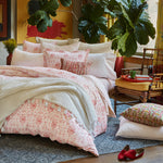 A Poseti Lotus Organic Sheet Set by John Robshaw in pink and white that is machine washable, on a bed. - 15522916073518