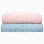 Two Vivada Blush Woven Quilts from Quilts & Coverlets, one pink and one blue, stacked on top of each other. - 28766027153454