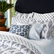 A Layla Indigo Quilt by John Robshaw adorns a bed with blue and white bedding, accompanied by a potted plant, reminiscent of Mughal gardens.