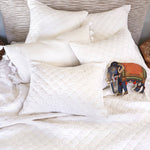 A reversible Layla White Quilt bed with cotton voile pillows and a stuffed elephant. - 28783174025262