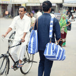 A man on a bicycle carrying a John Robshaw Vintage Stripe Duffle Bag. - 6601745891374
