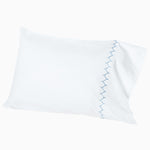 A white pillow with blue embroidered designs will be replaced with the Stitched Light Indigo Organic Sheets by John Robshaw. - 30252477677614