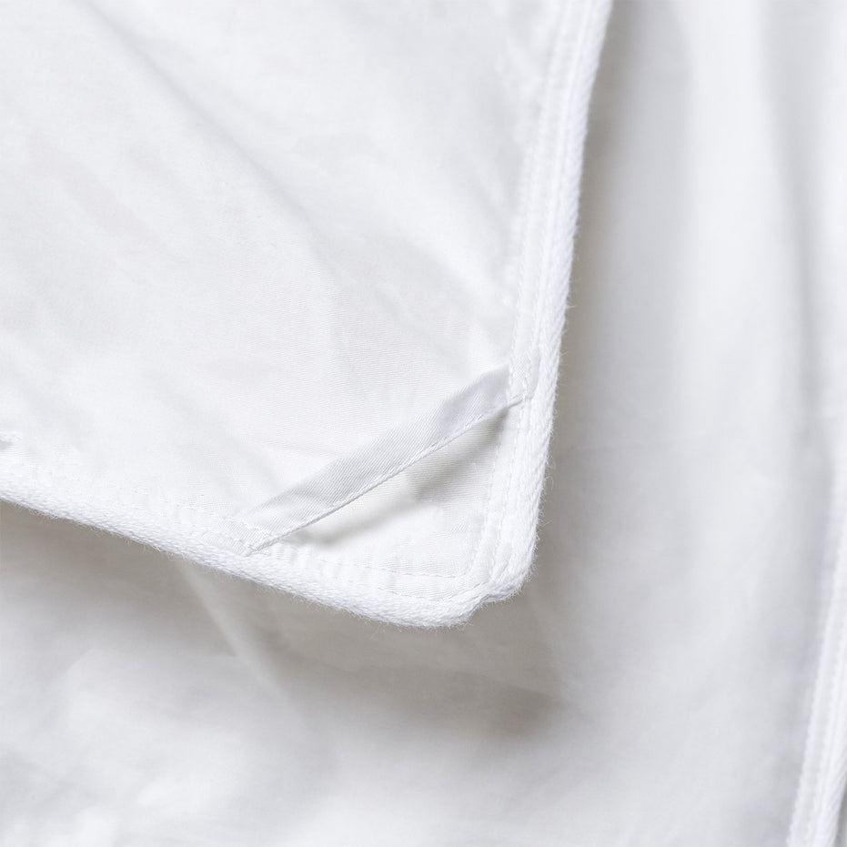 A close up of a John Robshaw white Down Comforter with a zipper, featuring baffle box construction.